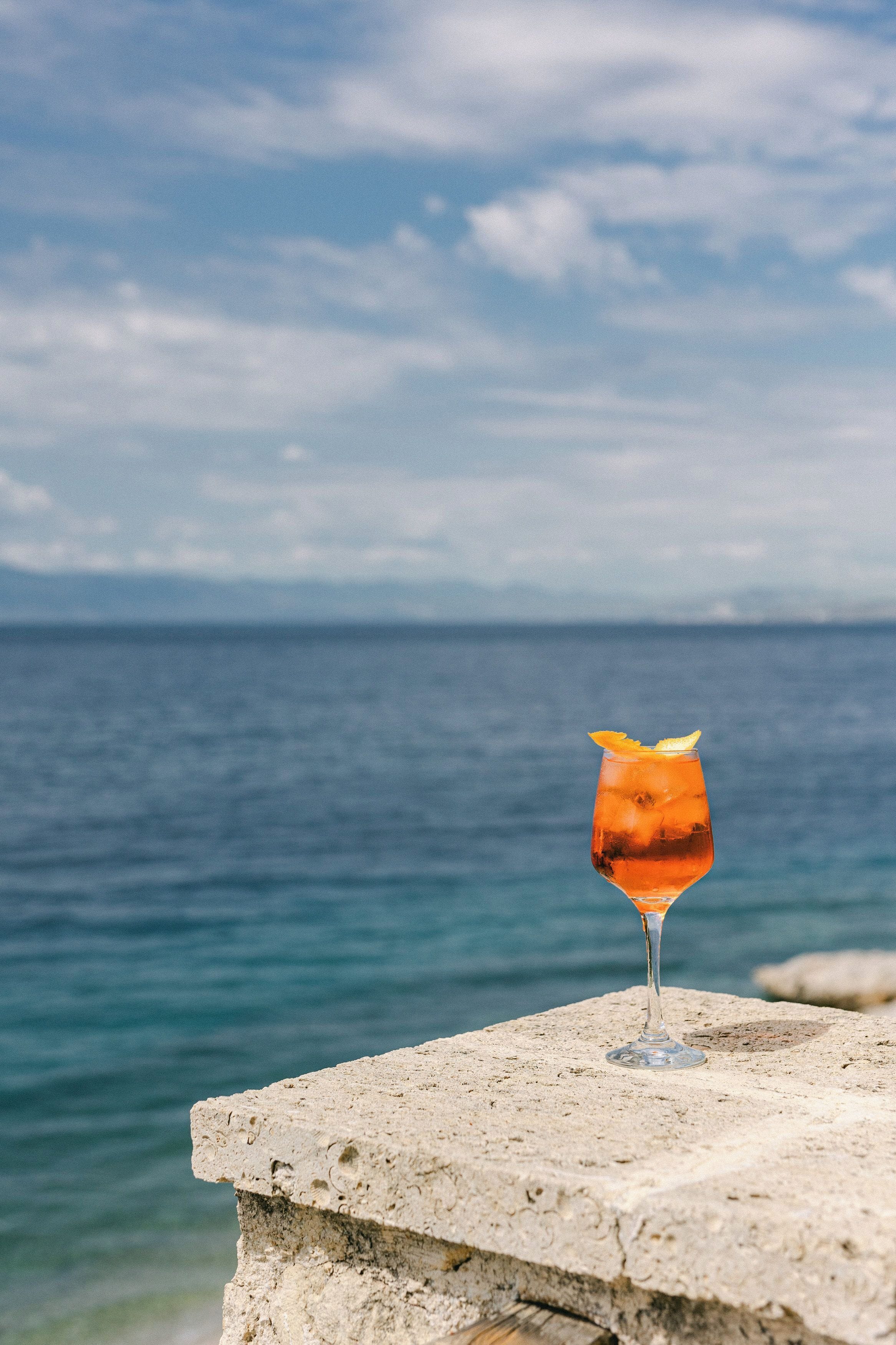 Ein Getränk in einem Glas auf einer Steinstufe mit Blick auf Meer und Himmel.