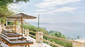 Une terrasse en bord de mer, dotée de chaises longues et d’une pergola en bois, offrant une vue sur la mer.