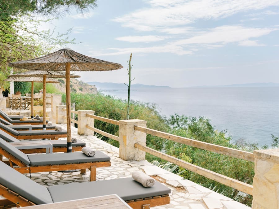 A seaside terrace with lounge chairs and a wooden pergola, overlooking the sea.