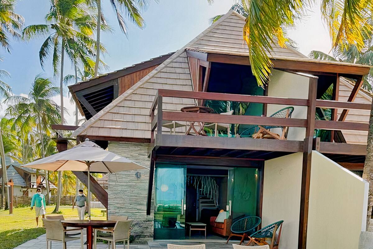 A modern pool area with two lounge chairs, a table with an umbrella, and a view of a two-story building with a sloped roof.
