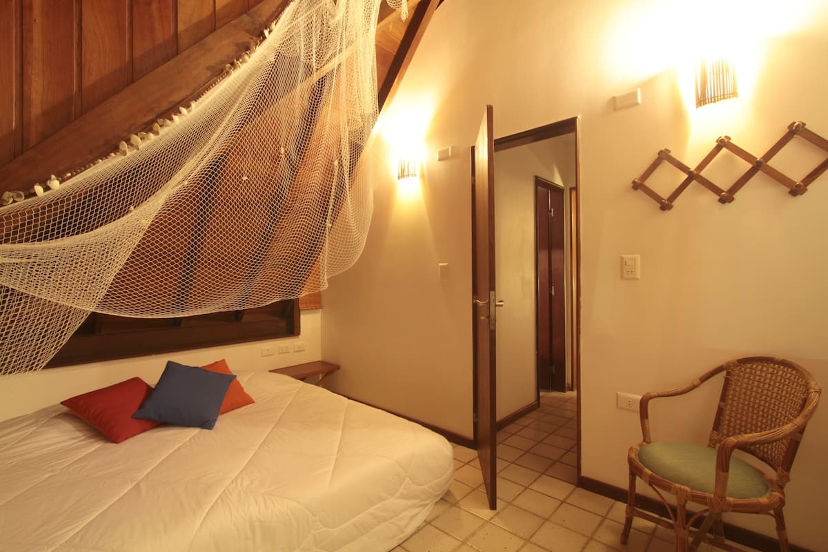 A bedroom with a bed, a chair, a door, and a wall-mounted light fixture.