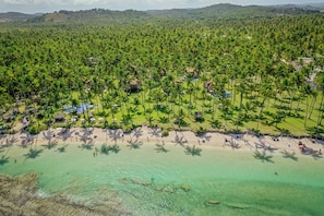 Vista aérea de un resort con playa, palmeras y aguas turquesas cristalinas.