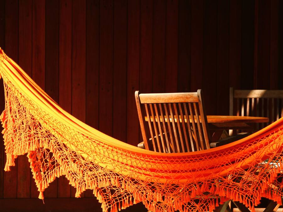 A hammock with a netted edge, a wooden chair, and a wooden wall in the background.
