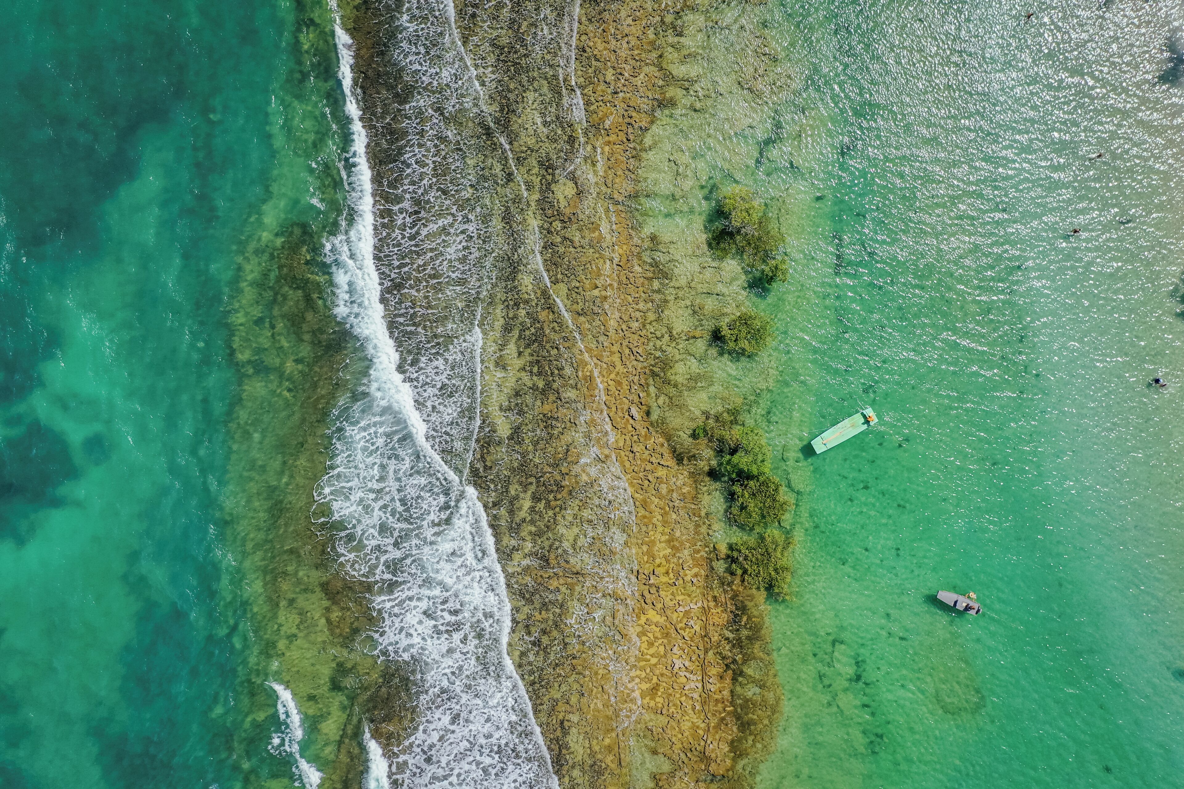 An aerial view of a coastal area with clear waters, rocky shoreline, and a boat.