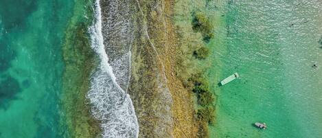 An aerial view of a coastal area with clear waters, rocky shoreline, and a boat.