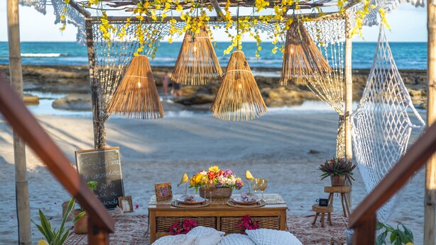 A beach setting with a wooden table adorned with flowers, a chalkboard, and a hammock. - Pontal dos Carneiros Beach Bungalows (Tamandaré)