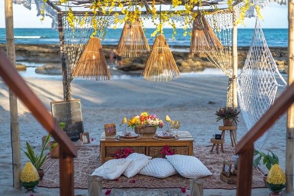 Eine Strandkulisse mit einem Holztisch, der mit Blumen, einer Kreidetafel und einer Hängematte geschmückt ist.