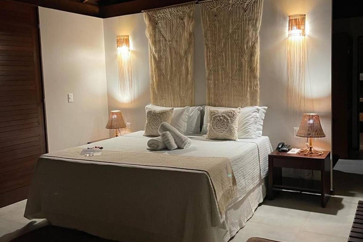 A bedroom with a wooden ceiling, a bed with white bedding, two bedside lamps, and a nightstand with a lamp.