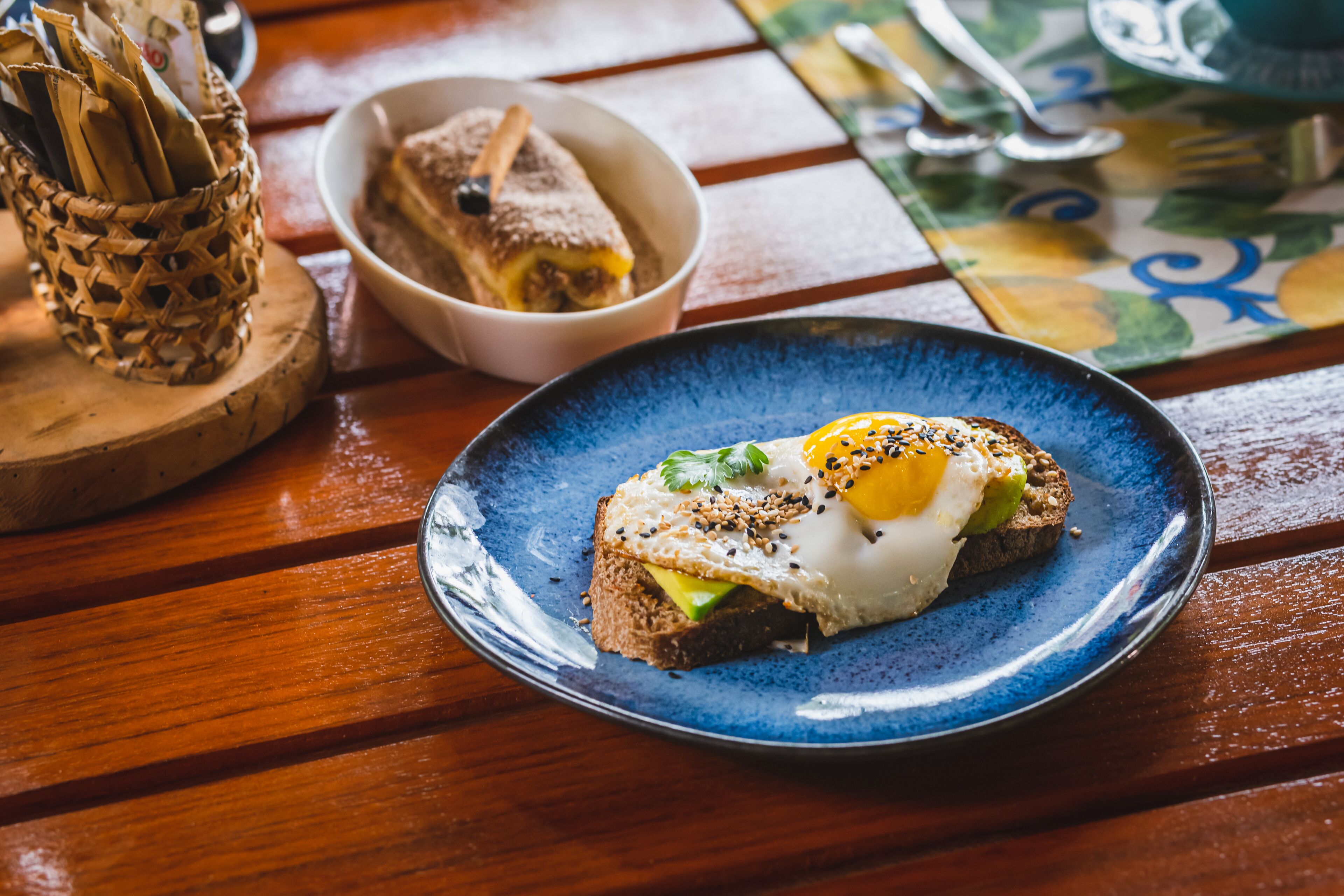 Une assiette de petit-déjeuner avec des toasts, de l’avocat, un œuf et des graines, le tout servi sur une assiette bleue.