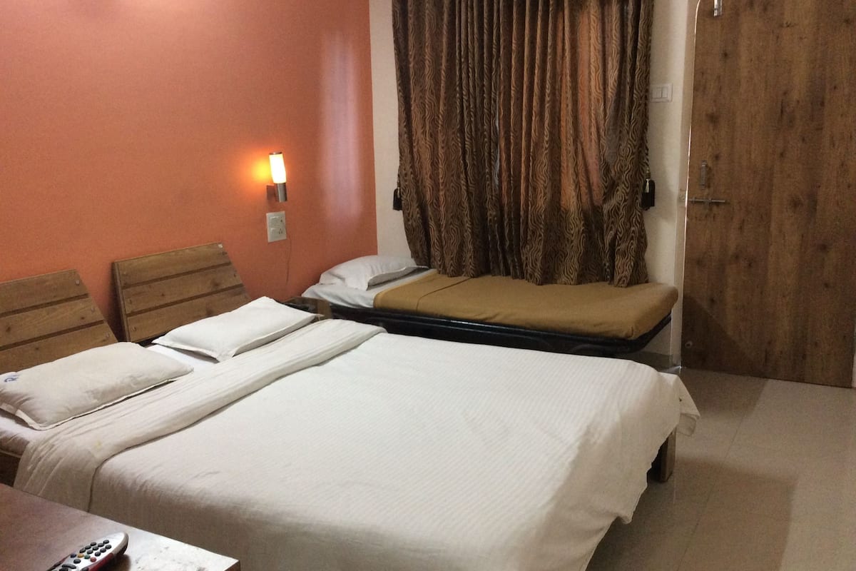 Een hotelkamer met twee bedden, een houten hoofdbord, een nachtkastje met afstandsbediening en een gordijn.