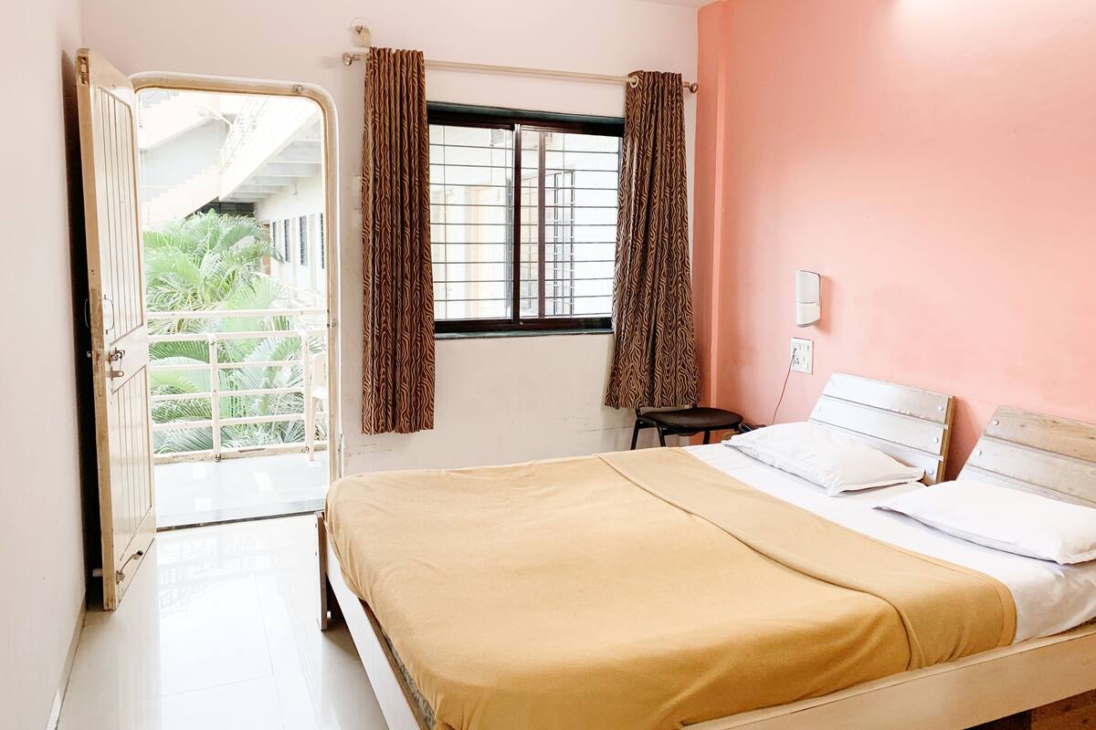 Een slaapkamer met een bed, een raam met gordijnen, een stoel en uitzicht op een balkon.
