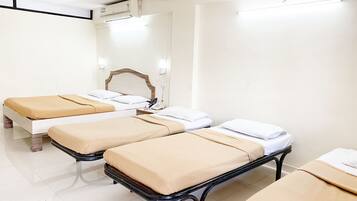 Three single beds with wooden headboards and bedside tables, a flat-screen TV, and air conditioning for a comfortable stay.