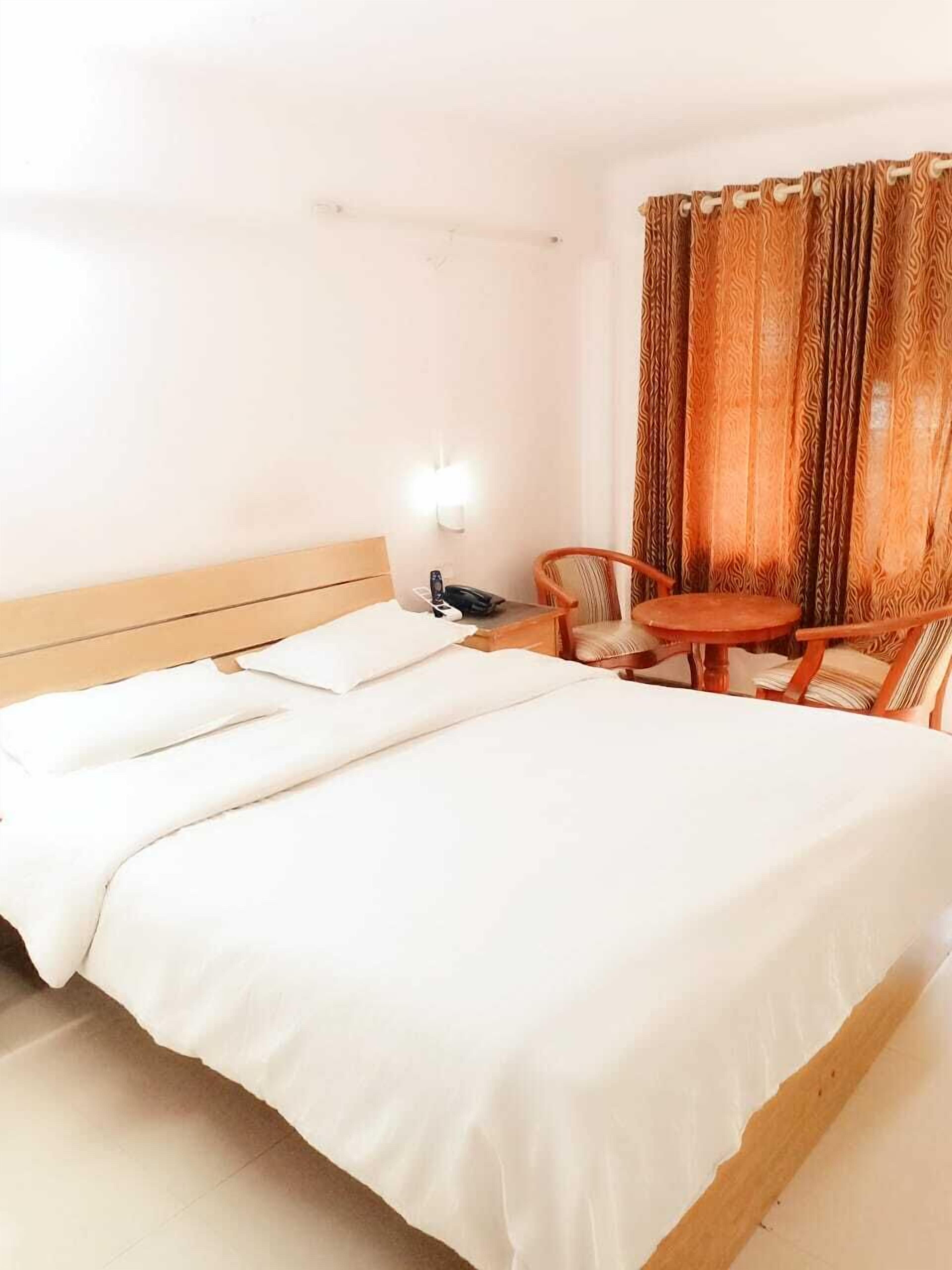 A hotel room with a large bed, a bedside table, a chair, and a small table.