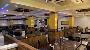 Un restaurante moderno con varias zonas de comedor, cada una con una mesa alta y sillas. Hay ventiladores de techo e iluminación empotrada.