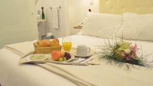 Una cama bien hecha con sábanas blancas, una bandeja de desayuno con cruasanes, fruta y jugo de naranja, y un ramo de flores.