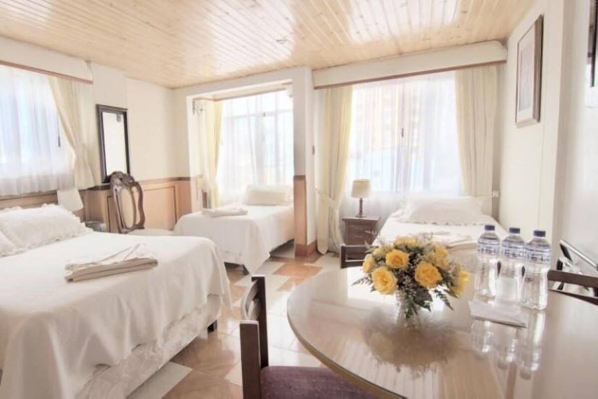 A hotel room with two beds, a sitting area with a table, and a large window.