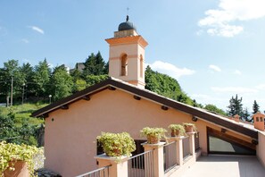 A building with a bell tower, a sloped roof, and potted plants on the balcony. - Relais Al Convento (Campello sul Clitunno)