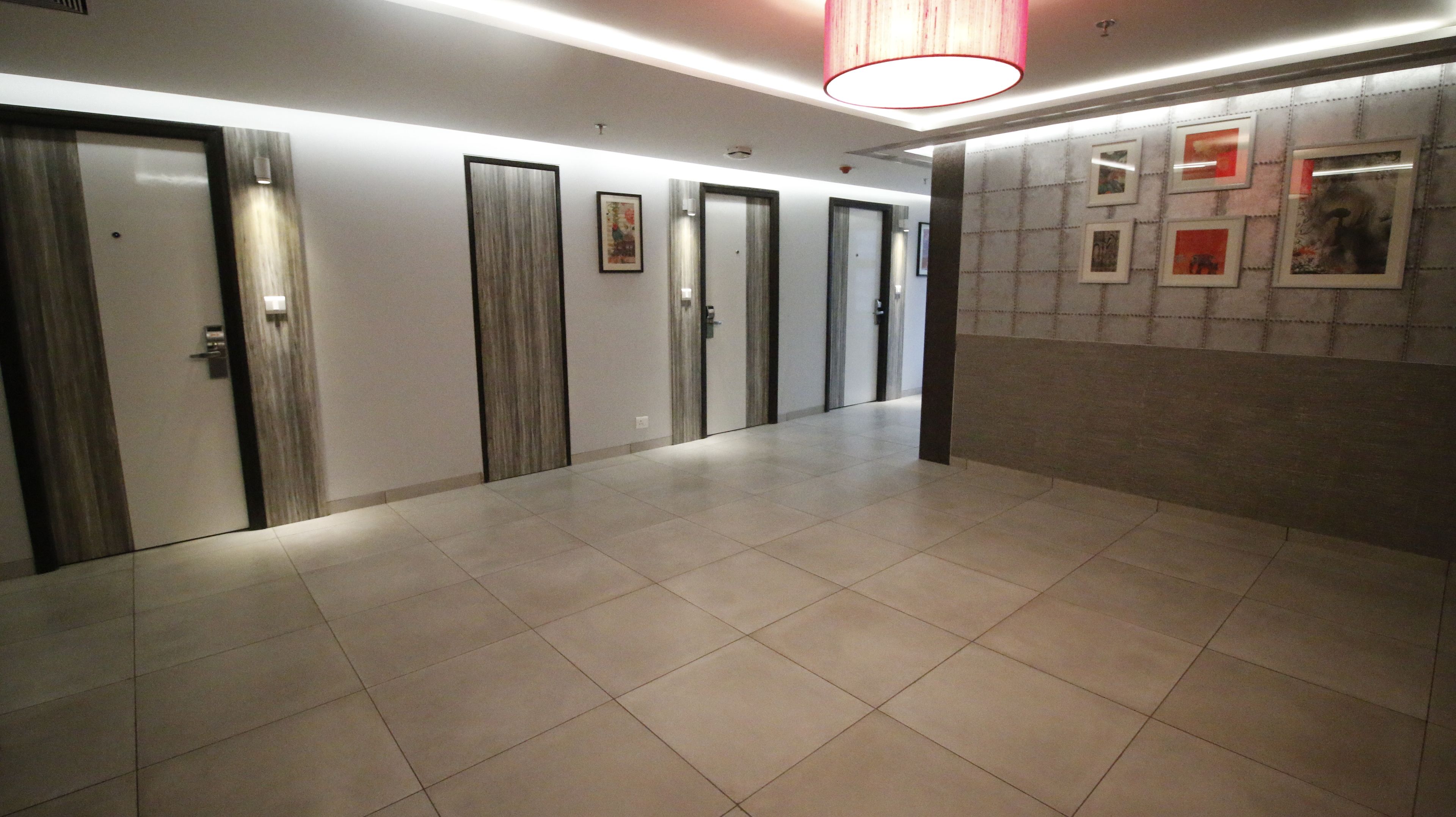 A hallway with a series of doors, a tiled floor, and a wall with framed pictures.
