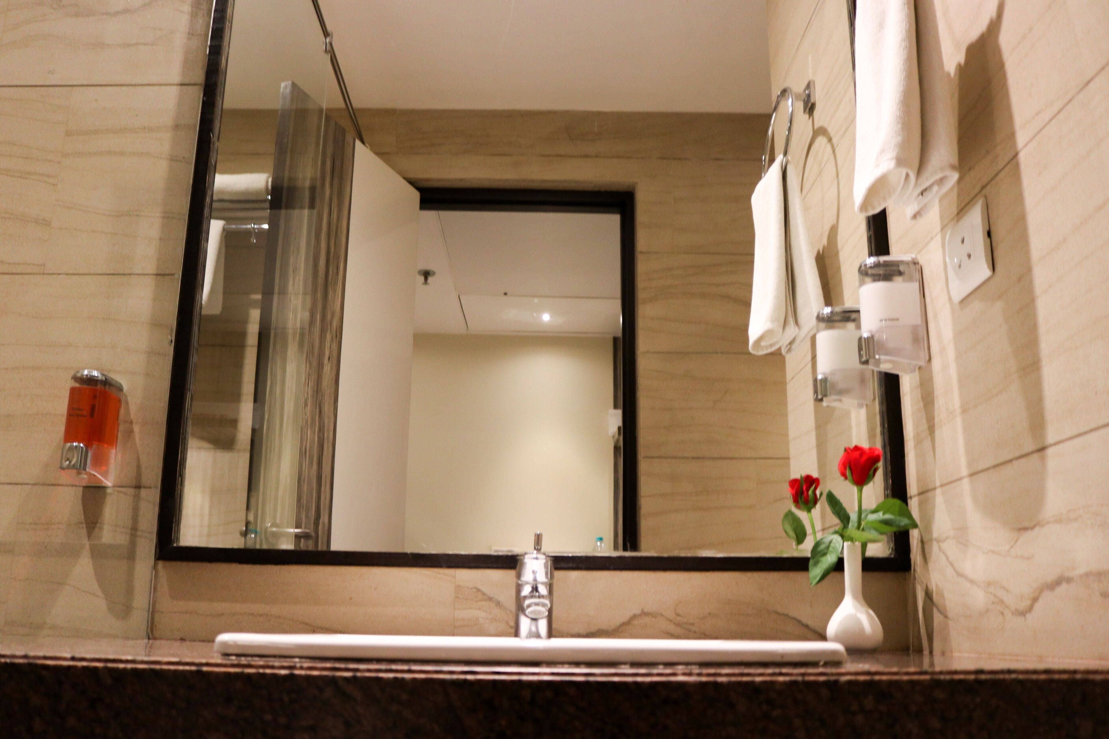 Un baño con lavamanos de mármol, un espejo grande y un florero con flores.