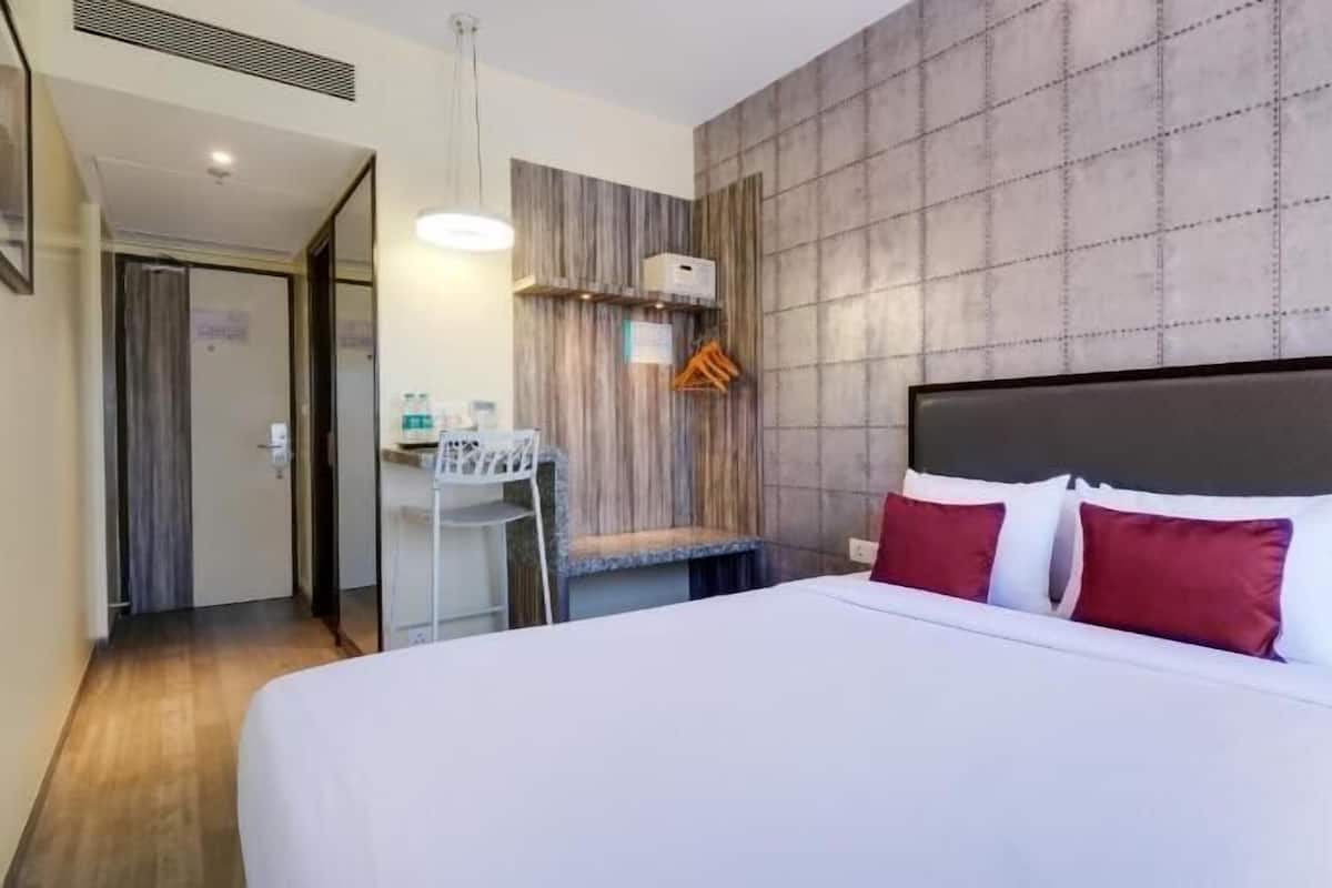 Quarto de hotel com uma cama grande, uma escrivaninha com cadeira, luminária pendente e parede texturizada.