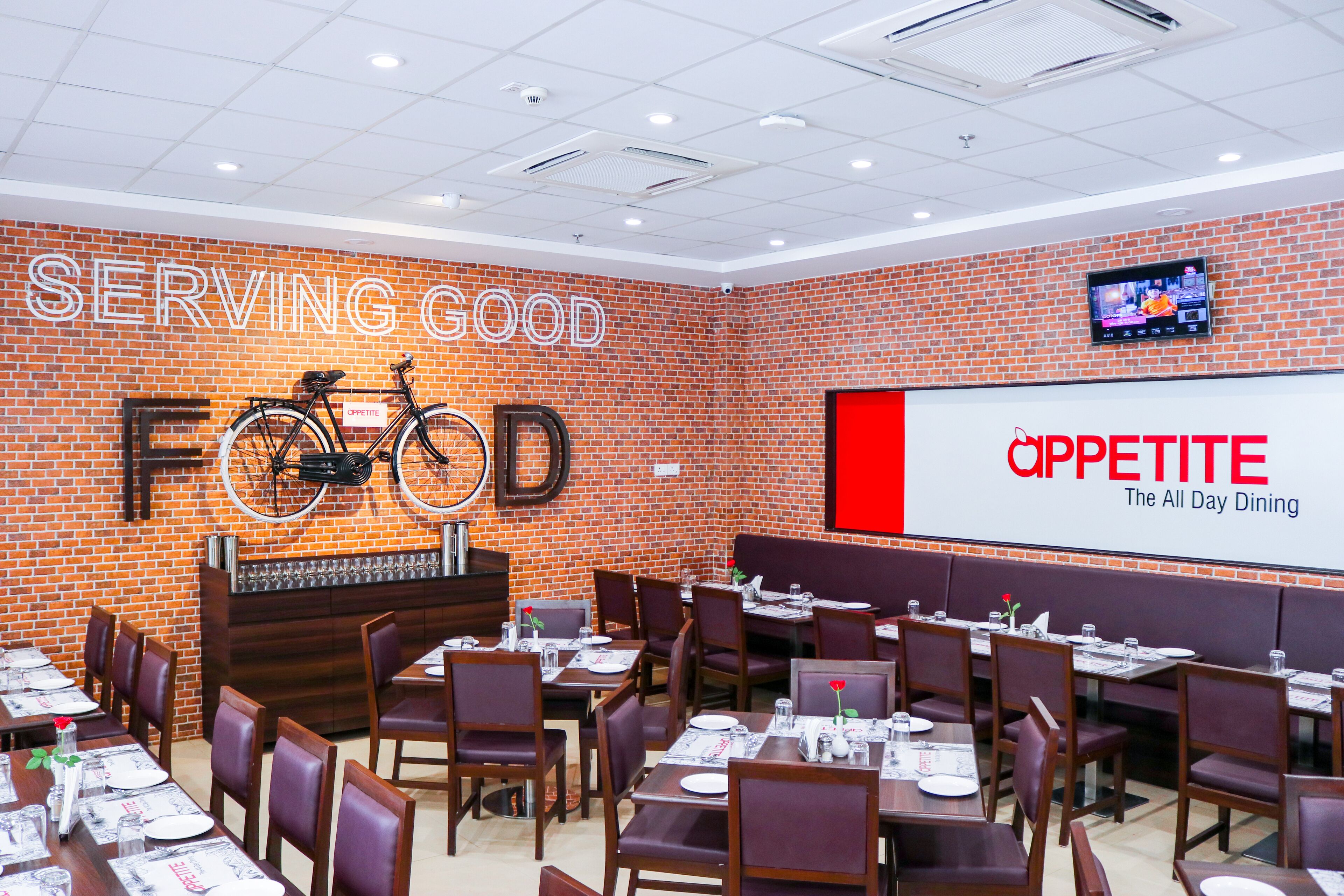 A restaurant interior with brick walls, multiple dining tables, and a large screen displaying the restaurant's name.