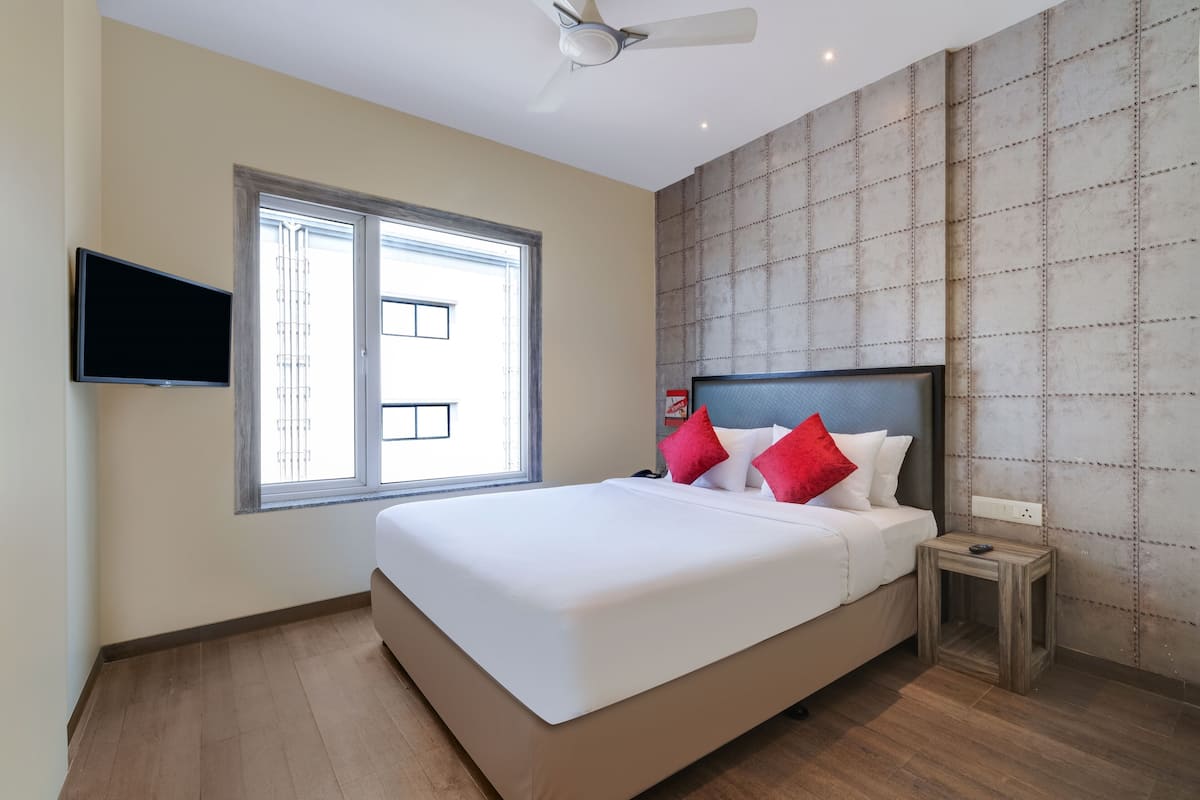 Quarto com cama grande, televisão fixada na parede e janela com vista para edifícios.