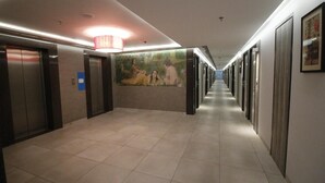 Ein Hotelgang mit Aufzügen, einem Wandgemälde und einer langen Halle mit Türen.
