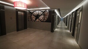 Ein Hotelgang mit einer großen Wandmalerei im Stil einer Uhr, Aufzügen und einem gefliesten Boden.