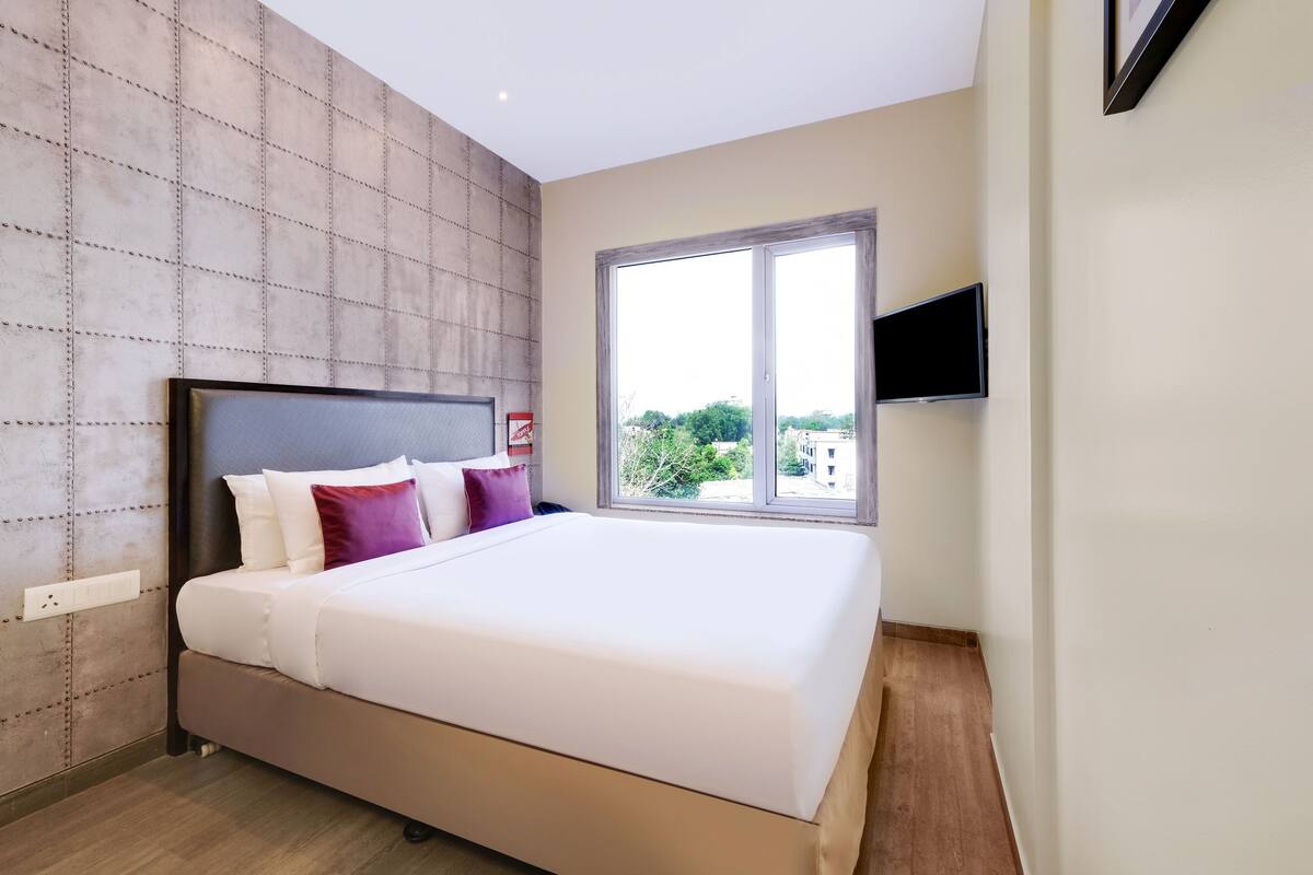 Quarto moderno com uma cama grande, televisão na parede e janela com vista para a cidade.