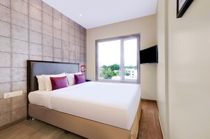 Un dormitorio moderno con una cama grande, un televisor montado en la pared y un ventanal con vistas a la ciudad.