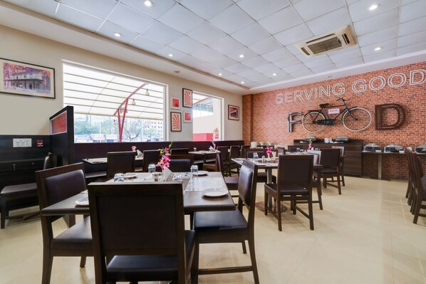 A restaurant with brick walls, multiple tables and chairs, and a sign that reads "SERVING GOOD FOOD". - 7 Apple Hotel Vadodara (Vadodara)