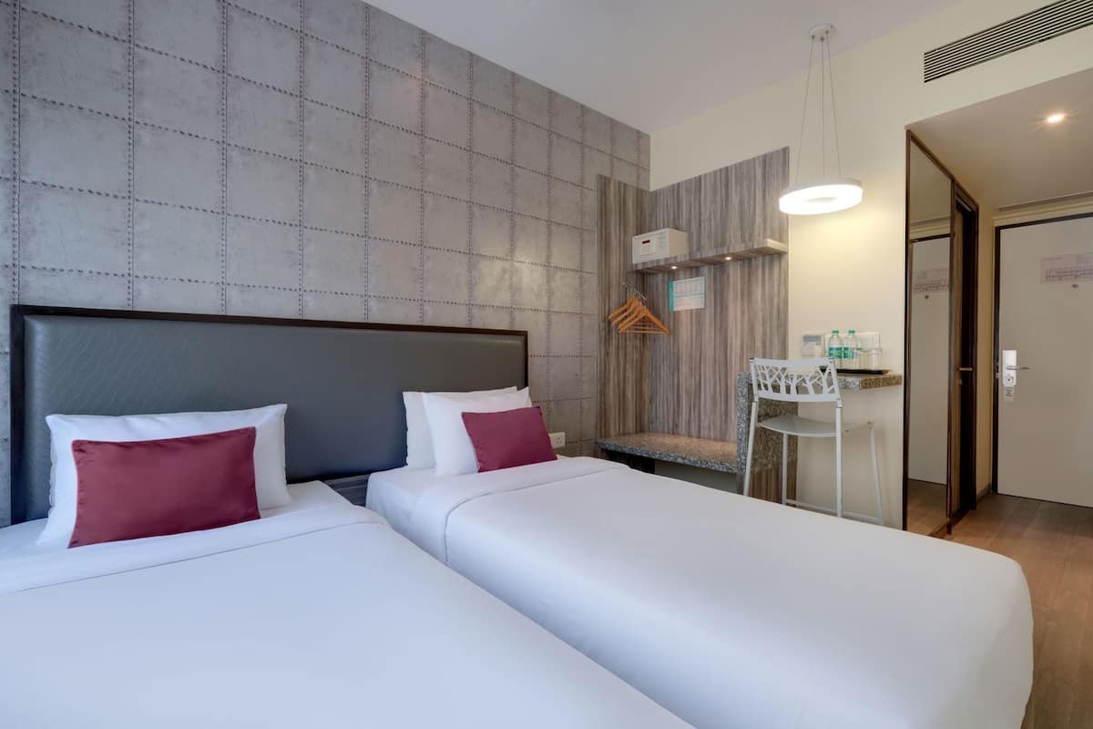 Quarto de hotel com duas camas, uma secretária pequena, uma cadeira e um guarda-roupa.