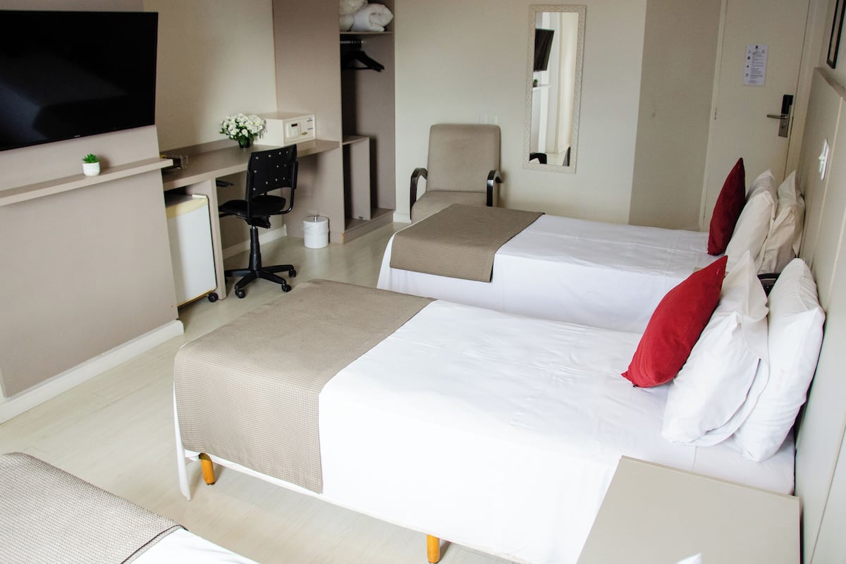 A hotel room with two beds, a desk, a chair, a TV, and a closet.