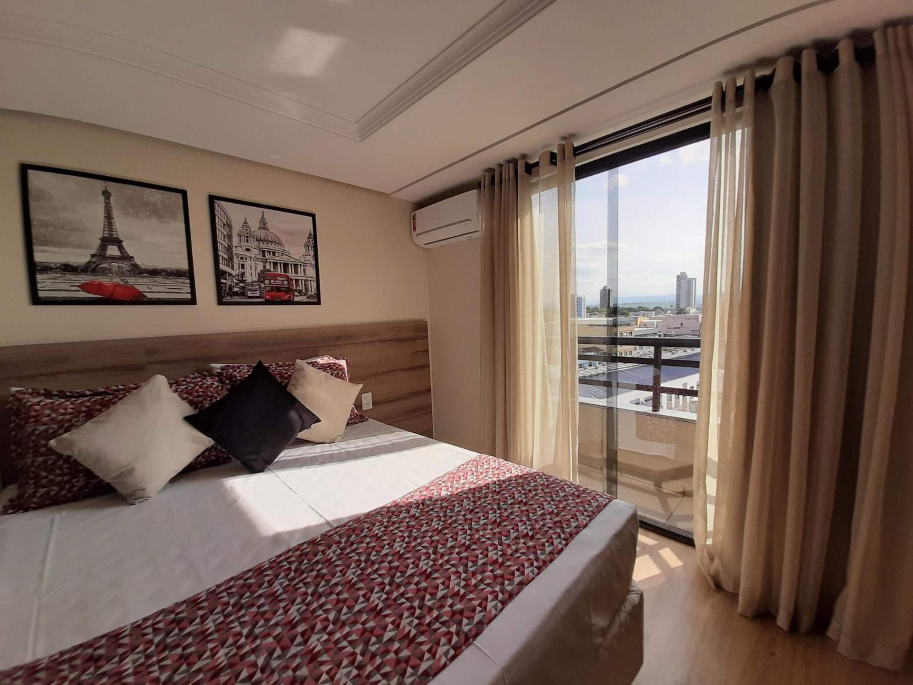 A hotel room with a bed, a cityscape view, and two framed pictures on the wall.