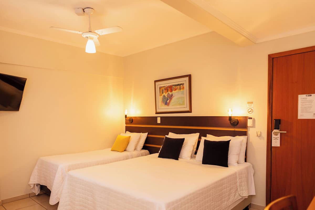 A hotel room with two beds, a ceiling fan, a painting on the wall, and a door with a sign.