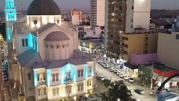 A large church with a prominent dome and two towers, surrounded by modern buildings and a parking area with cars.