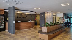 A hotel reception area with a check-in counter, a clock, and a plant display. - Hotel Ferraz (Pouso Alegre)