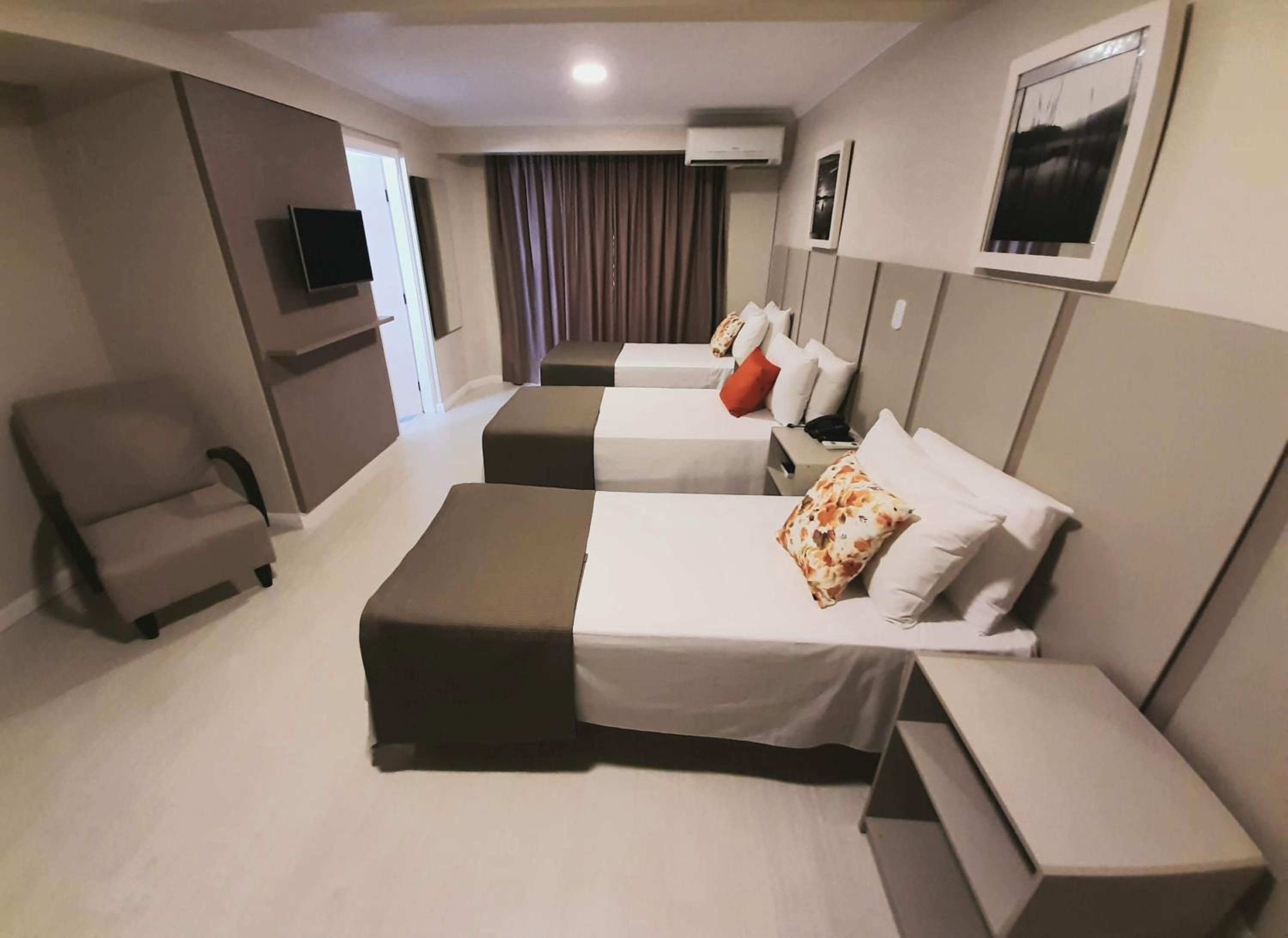 A hotel room with two beds, a chair, a flat-screen TV, and a wall-mounted air conditioner.