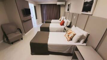 A hotel room with two beds, a chair, a flat-screen TV, and a wall-mounted air conditioner.