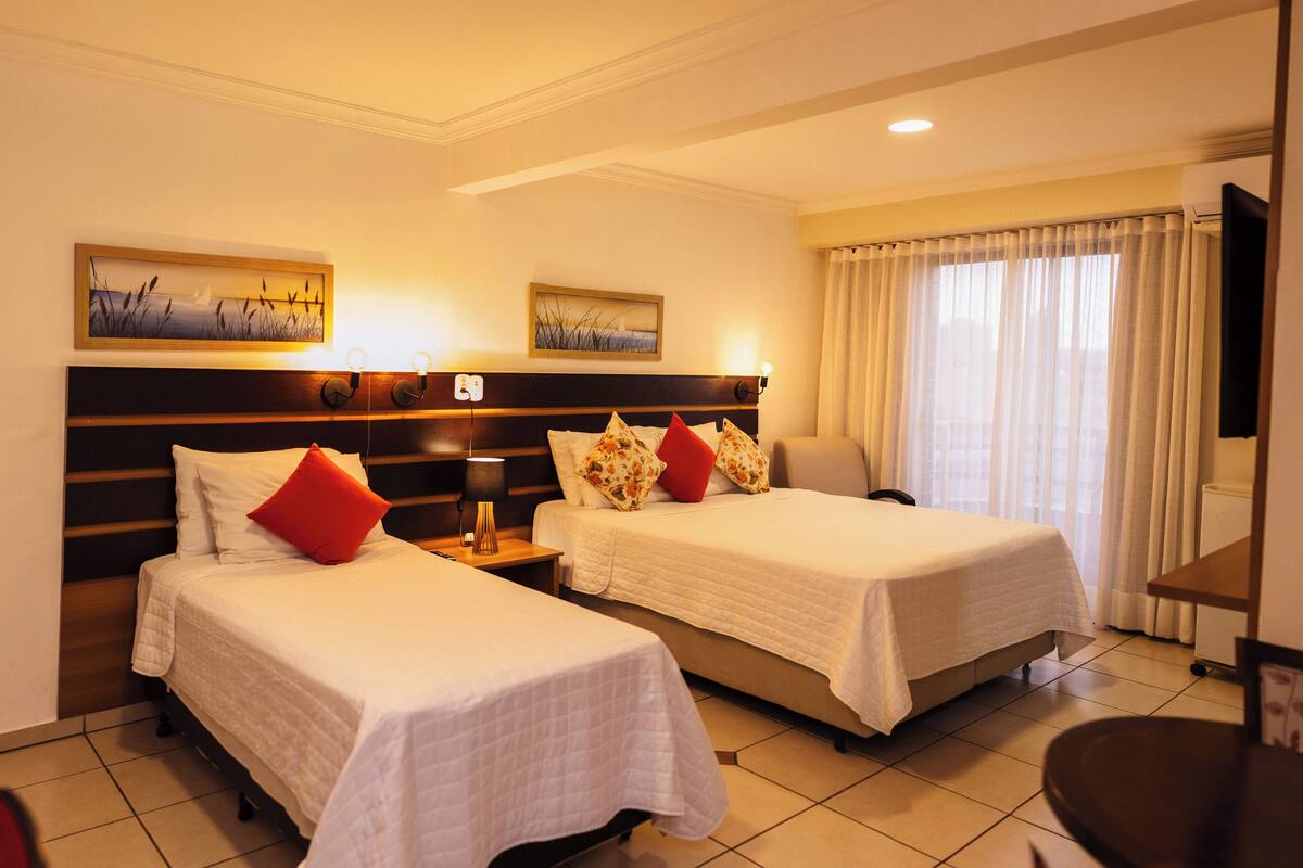 A hotel room with two beds, a flat-screen TV, and artwork on the walls.