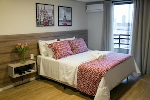 Una habitación de hotel con una cama, una mesita de noche con un jarrón de flores y dos cuadros en la pared.