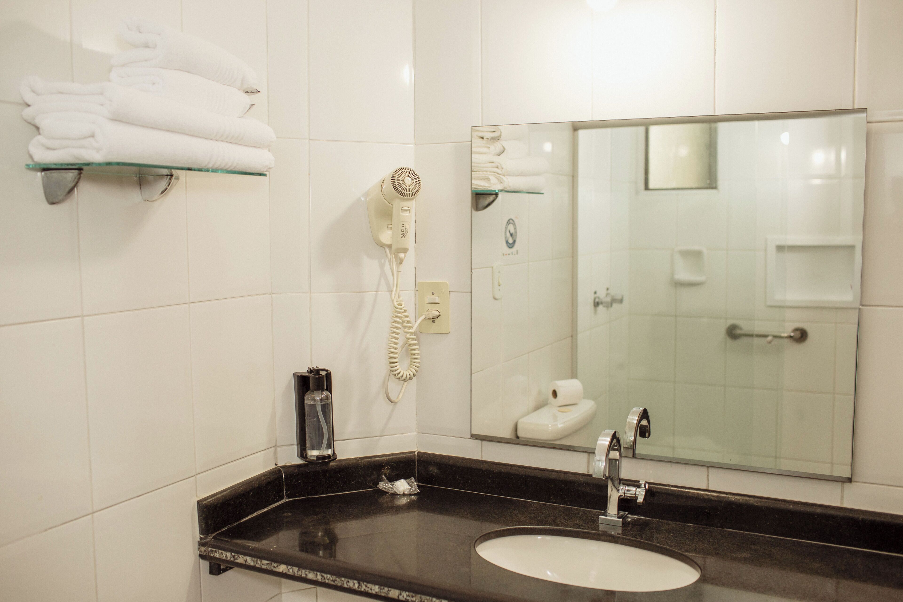 Un baño con encimera negra, lavamanos blanco y cabina de ducha de cristal.