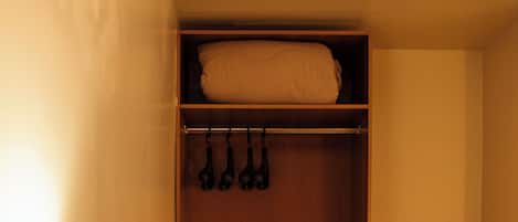Habitación de hotel con un escritorio de madera, una lámpara, una silla, un armario con ropa colgada y piso de baldosas.