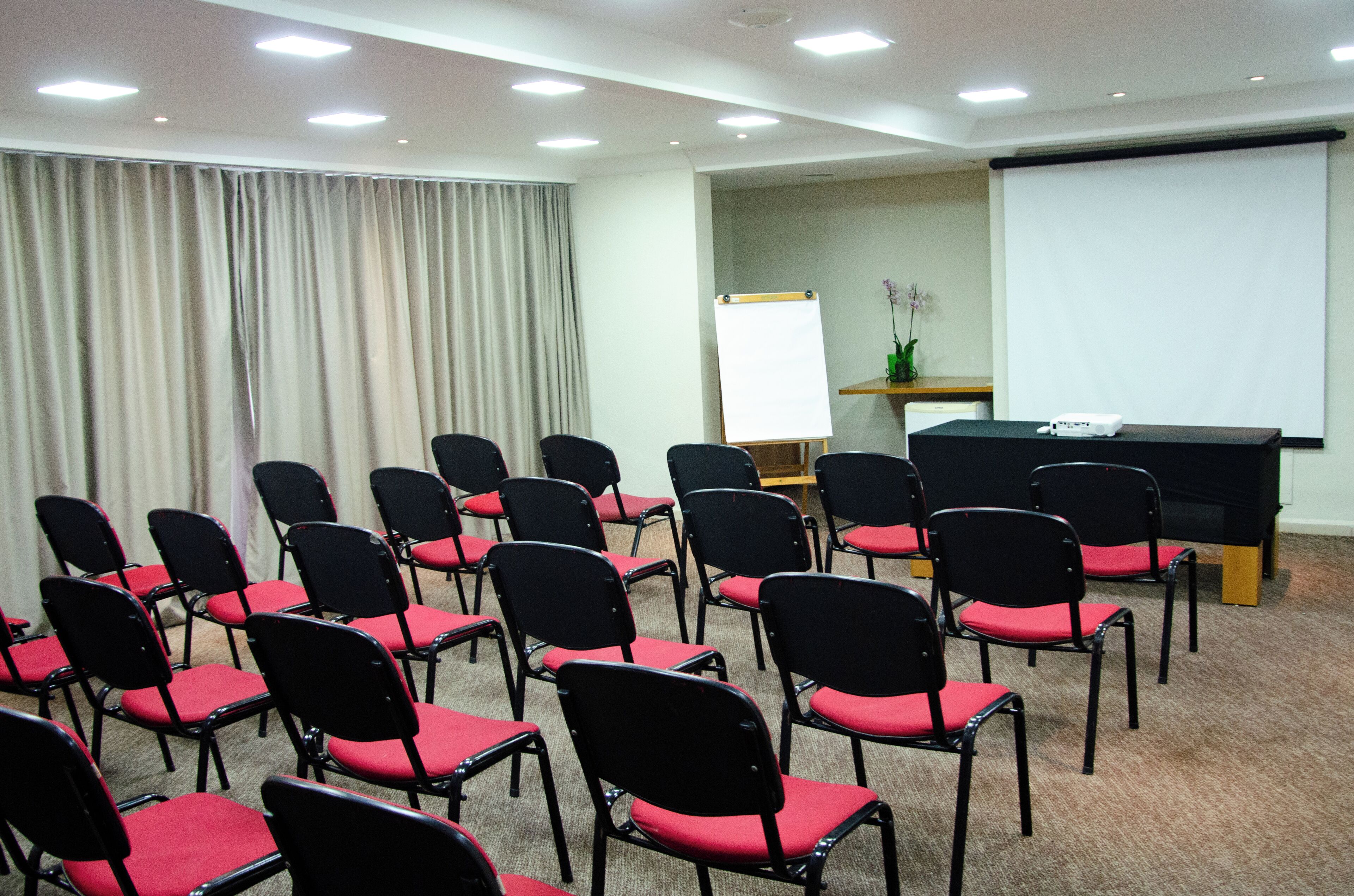 A conference room with rows of black chairs with red cushions, a whiteboard, and a projector on a stand.