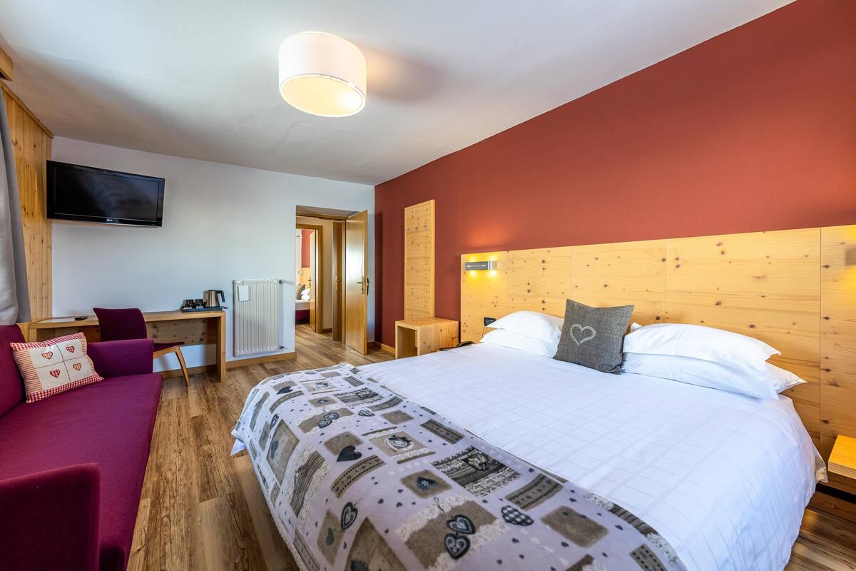 Hotellihuone, jossa on suuri sänky, työpöytä, televisio ja puinen pääty.