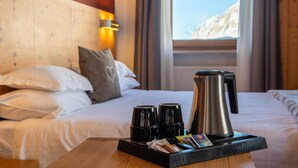 A hotel room with a bed, pillows, a tray with coffee cups, a kettle, and a window with a view of a mountain. - Hotel Col Di Lana (Canazei)