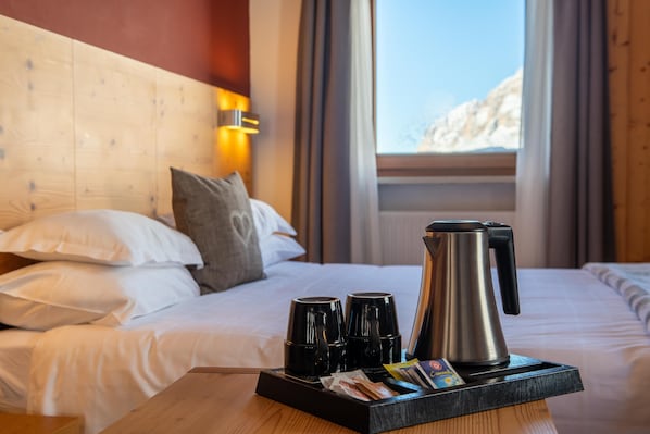 A hotel room with a bed, pillows, a tray with coffee cups, a kettle, and a window with a view of a mountain.