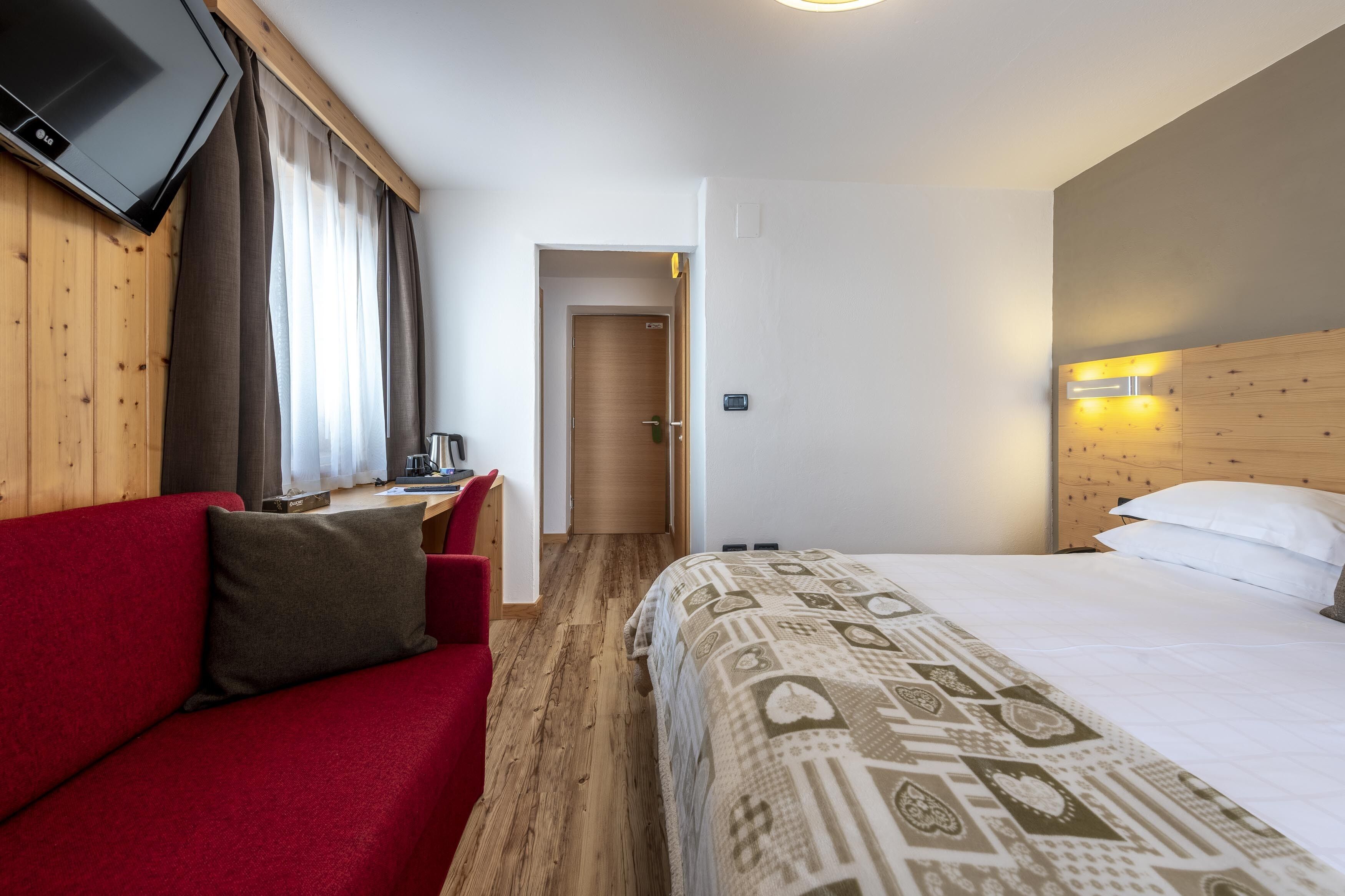 Ein Hotelzimmer mit rotem Sofa, einem Bett mit gemusterten Betttextilien, einem an der Wand befestigten Fernseher und einem hölzernen Kopfteil.