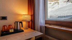 A cozy room with a wooden table, a lamp, and a window with a snowy mountain view. - Hotel Col Di Lana (Canazei)