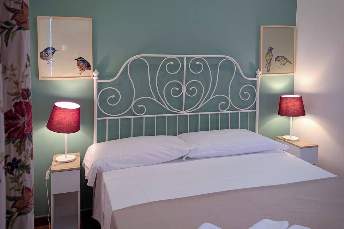 A neatly made bed with white linens, two bedside lamps with red shades, and floral curtains.